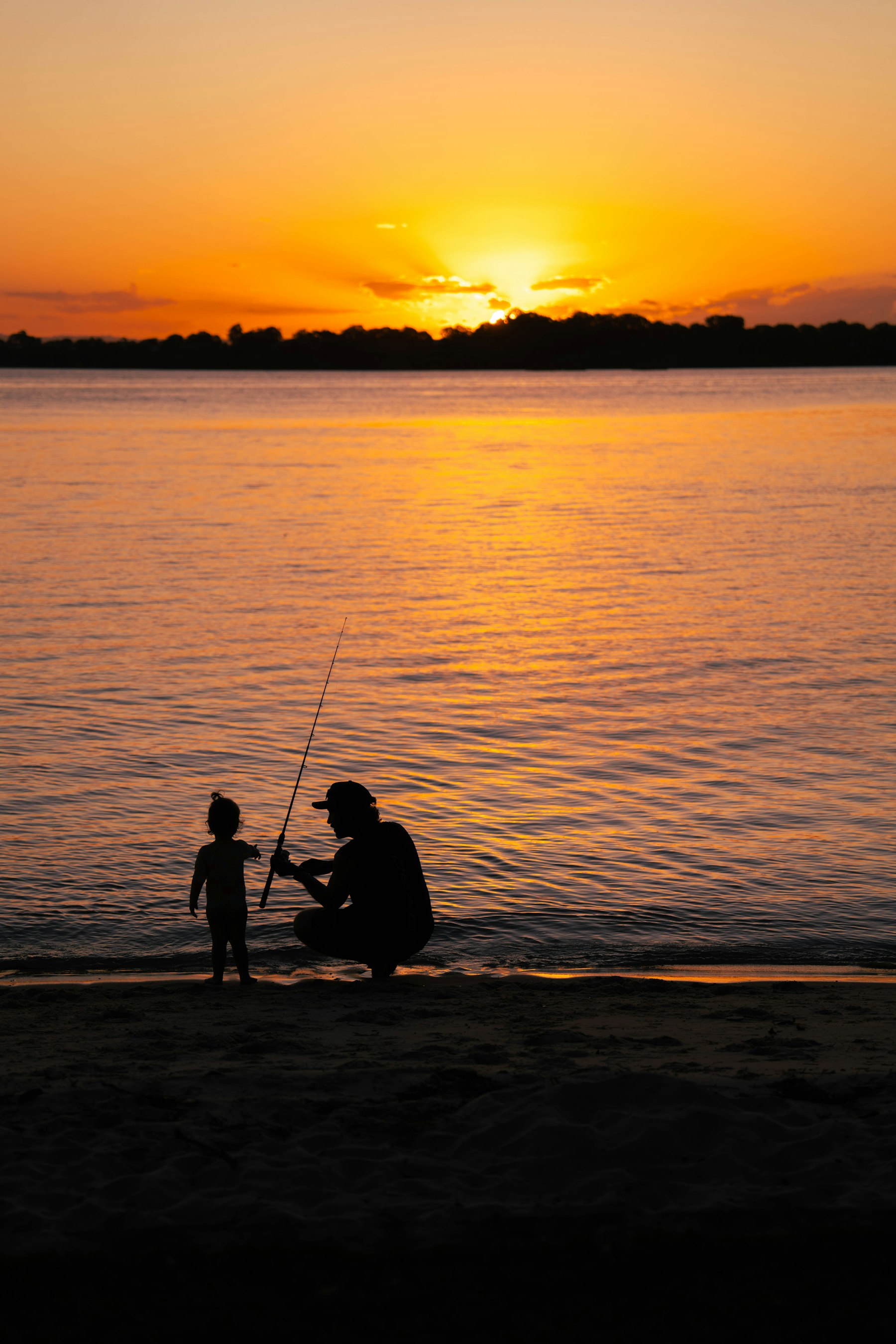 Father teaching his toddler to hold a fishing rod at sunset
